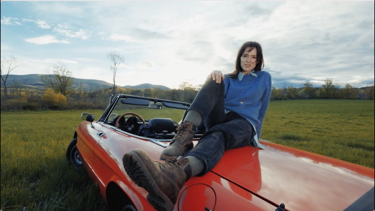 Emi Night sitting on a red convertible in an open field