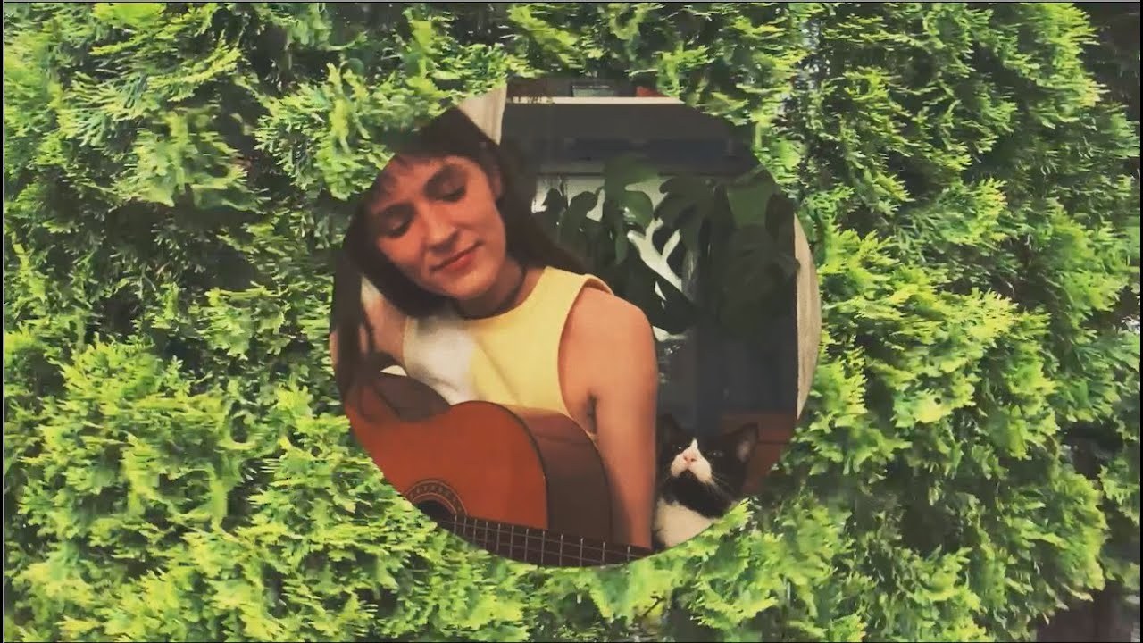 Emi Night lying in deep green foliage with a guitar